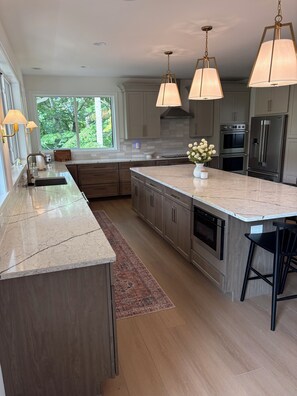 Una cocina moderna con una isla grande, electrodomésticos de acero inoxidable e iluminación colgante.