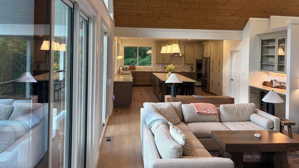 Un interior moderno con techo de madera, una cocina con isla central y una zona de estar con sofá y mesa baja.