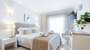 Moderni hotellihuone, jossa on sänky, yöpöydät, työpöytä, televisio ja huonekasvi.