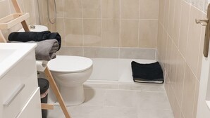 Een kleine badkamer met toilet, douche en een houten bankje.