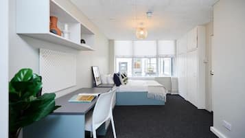 Ein modernes Schlafzimmer mit Schreibtisch, Bett, großem Fenster und Deckenleuchte.