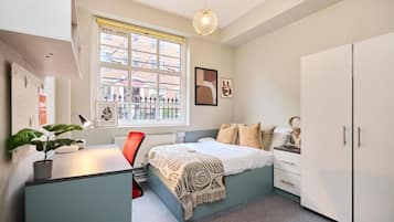 A bedroom with a bed, a desk, a chair, a wardrobe, a window, and a hanging light fixture.