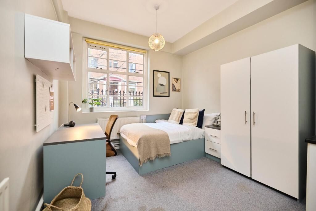 Een slaapkamer met een bed, bureau, stoel, kledingkast en een raam met uitzicht.