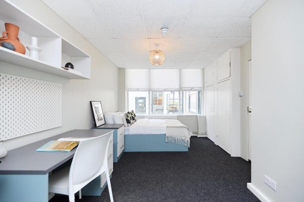 A room with a bed, a desk, a chair, a window, and a door.