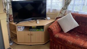 A living room with a television, a Scrabble game box, a sofa, and a table. - Caravan Sleeps 8 - Parking, Pet Friendly (Skegness)