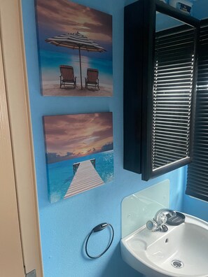 Et badeværelse med blå vægge, en hvid vask og to billeder i rammer med motiver fra stranden.