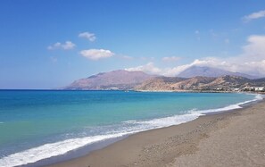 A beach with clear water, a mountain in the background, and a small boat. - Elmara - Beachside Lux Villa 2 With Private Pool (Faistos)