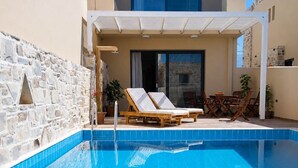 A swimming pool with lounge chairs, a stone wall, and a building with a balcony. - Elmara - Beachside Lux Villa 2 With Private Pool (Faistos)