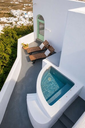 Ein moderner Poolbereich im Freien mit Whirlpool, Liegestühlen und Blick auf ein weiß getünchtes Dorf.