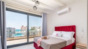 A bedroom with a large sliding glass door, a red upholstered bed, a white bedside table, and an air conditioning unit on the wall. - Elmara Lux Seaside Villa 1 Private Pool in Crete (Faistos)