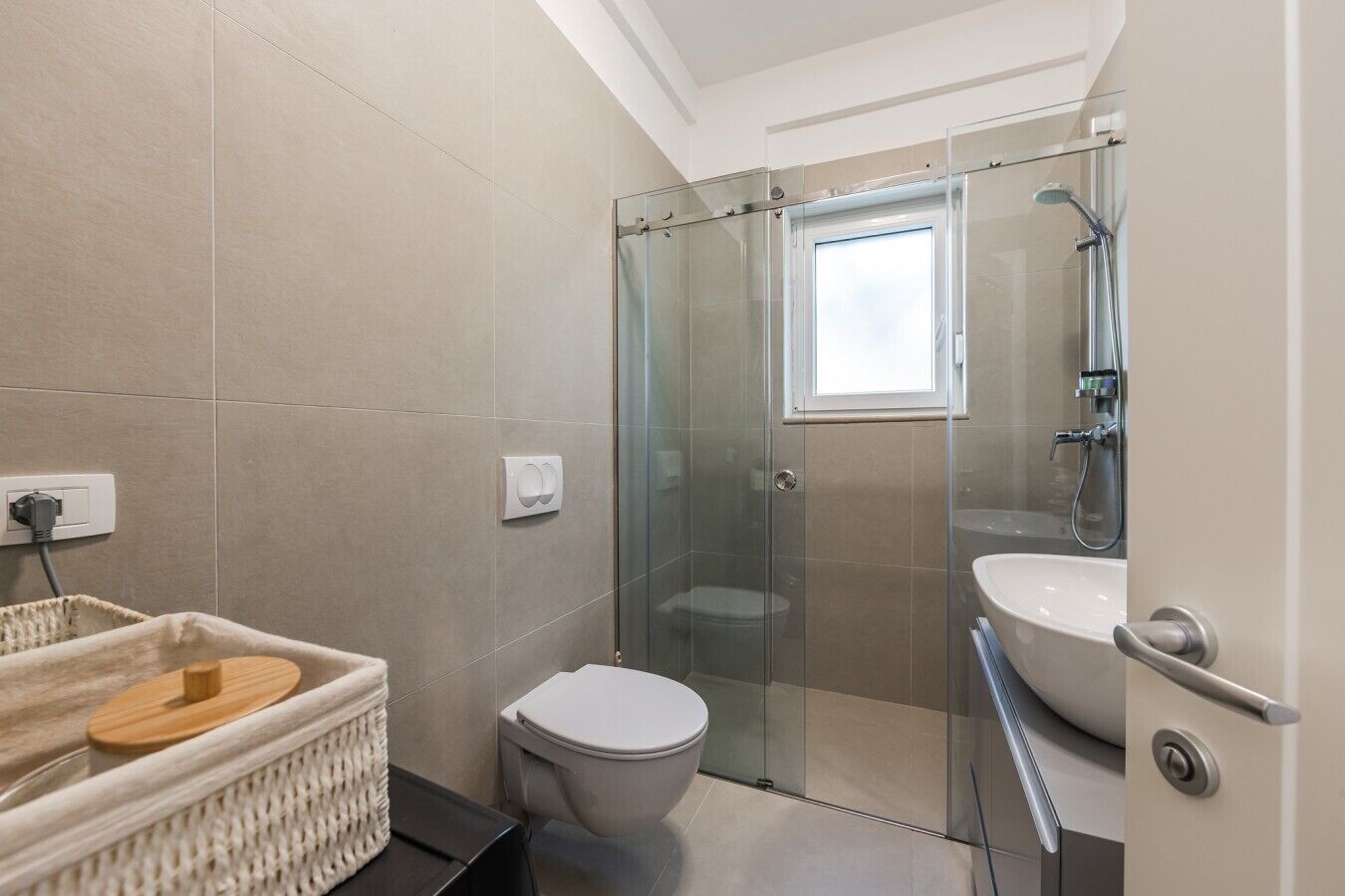 Un baño moderno con ducha de vidrio, inodoro blanco y un lavamanos grande.