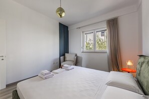 Una habitación de hotel con una cama, una silla, una ventana con cortinas y una mesita de noche con lámpara.