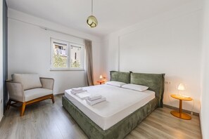 A bedroom with a bed, a chair, a window, and bedside lamps.
