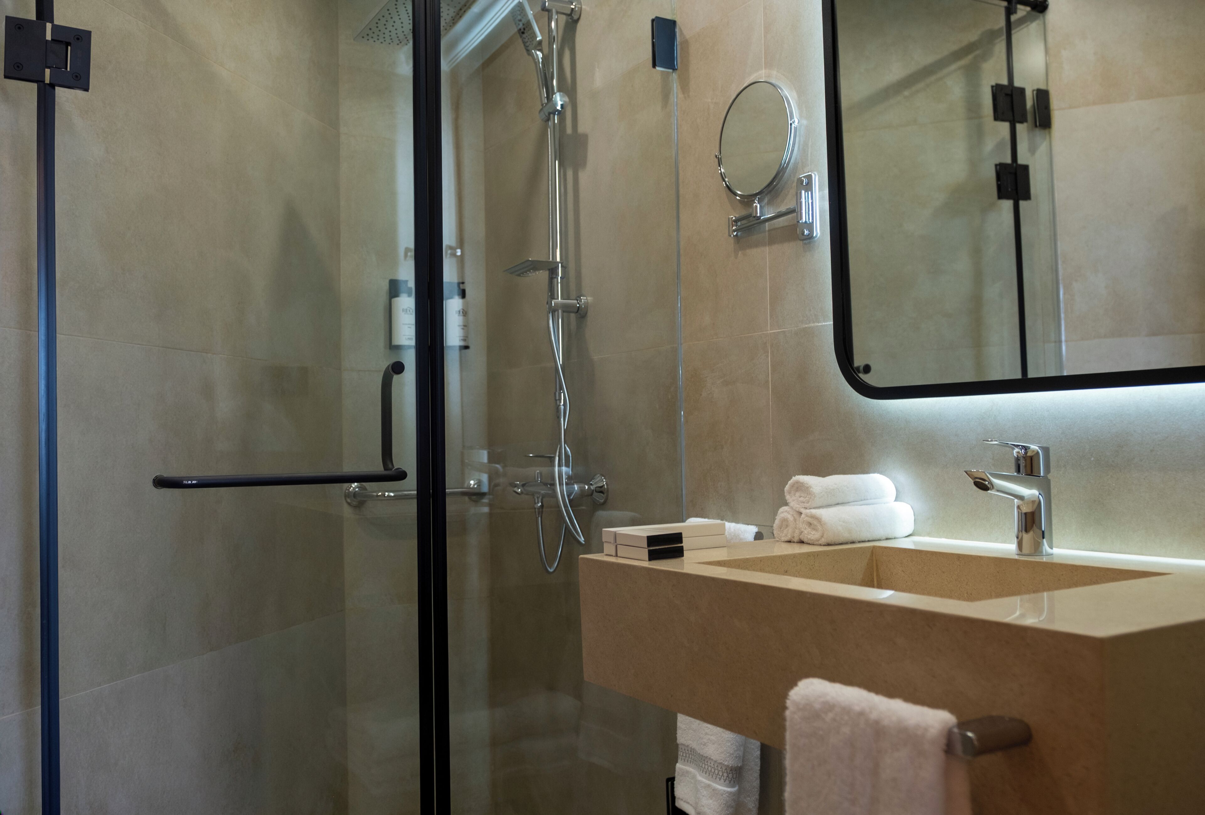 Un baño moderno con cabina de ducha de vidrio, un lavamanos con espejo y toallas ordenadamente dobladas.