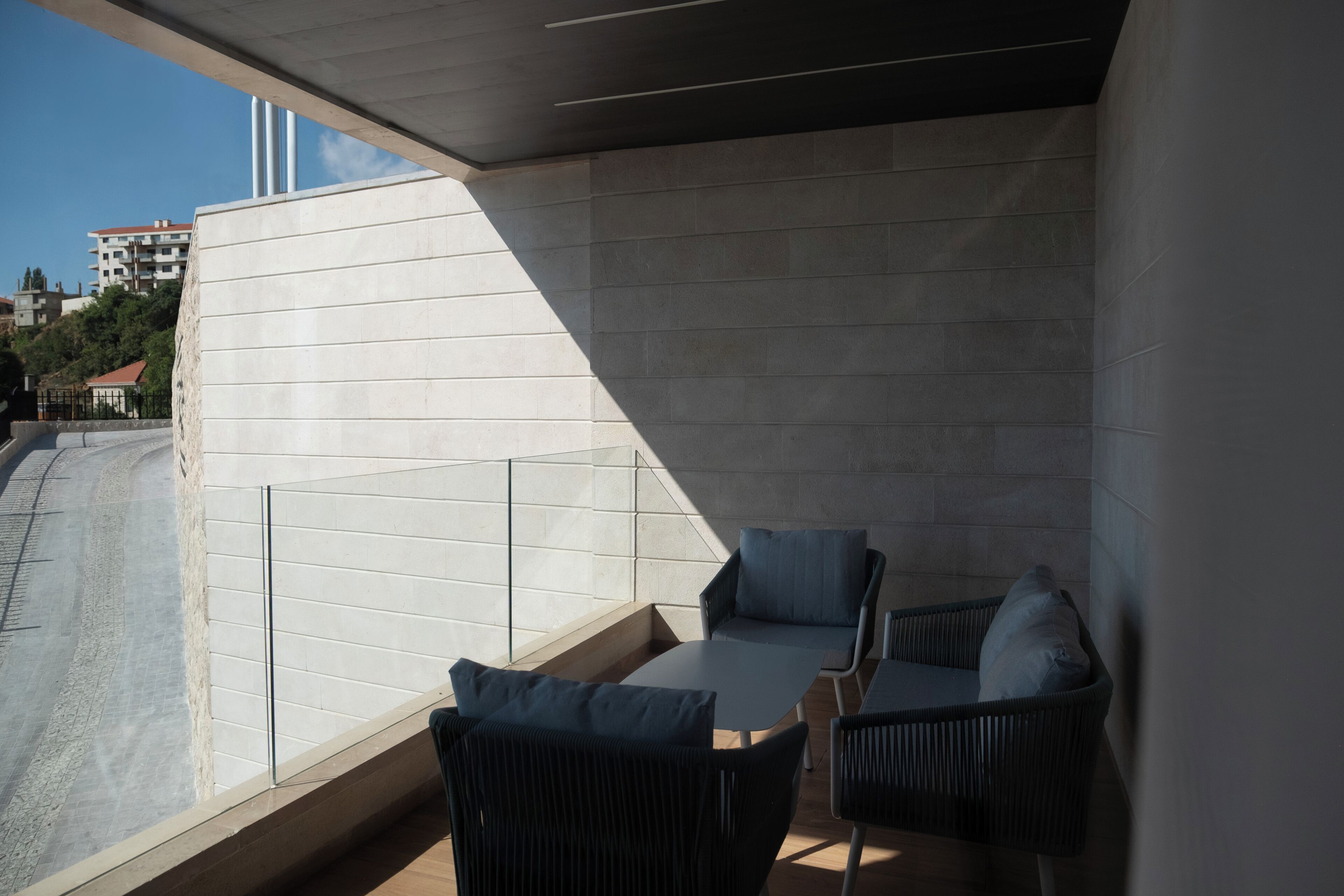 Un balcón con dos sillas y una mesa, un muro de azulejos y vistas a edificios al fondo.
