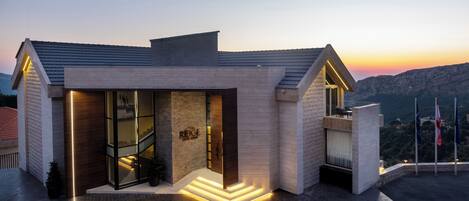 A modern hotel with a glass facade, a stone exterior, and a balcony with a view of the landscape.