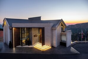 A modern hotel with a glass facade, a stone exterior, and a balcony with a view of the landscape.
