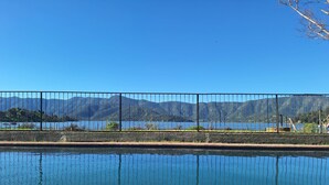 Krystalklart udsyn til en swimmingpool med et hegn, en rolig sø og bjerge i baggrunden.