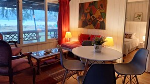 Et hyggeligt værelse med spisebord, stole, sofa og seng. Der er et vindue med udsigt.