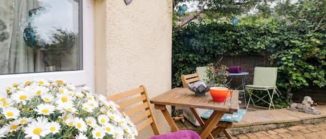 Une terrasse avec une table en bois, des chaises, une serviette violette et un arrangement floral.