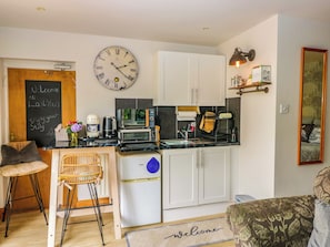 Cocina compacta con armarios blancos, microondas, cafetera y un reloj en la pared.