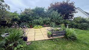 Un jardín con patio empedrado, plantas variadas y un banco.