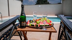 A bottle of Lussory Zero champagne, a glass of water, and a fruit platter with grapes and watermelon slices on a table by a poolside. - Private Luxury Villa with Pool, River Views (Shkodër)