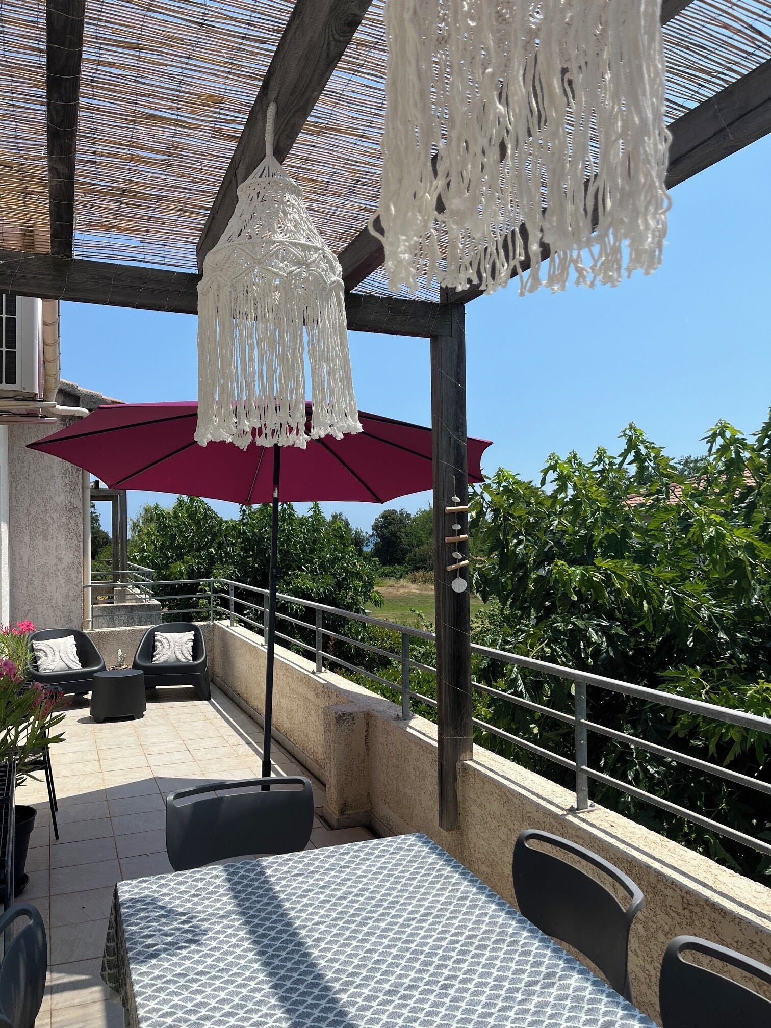 Eine Terrasse im Freien mit Tisch und Stühlen, einem roten Sonnenschirm und einer hängenden Lampenschirm aus Makramee.