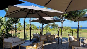 Een houten terras met buitenmeubilair, waaronder banken en stoelen, onder grote parasols.
