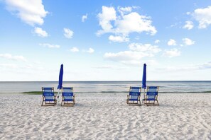 A beach with four blue lounge chairs and matching umbrellas, arranged in a row facing the ocean. - White Caps 505 by Liquid Life (Orange Beach)