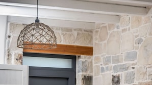 A dining area with a wooden table and white chairs, a stone wall, and a black door. - Elmara Crete Beachside Villa 3 With Private Pool (Faistos)