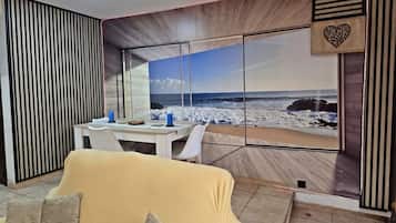 Een kamer met een groot raam met uitzicht op de oceaan, een eethoek en een zithoek.