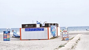 Club deportivo frente a la playa con un cartel, una pequeña estructura y un camino.
