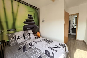 A bedroom with a bed, a wall with a stack of stones, and a door leading to another room.