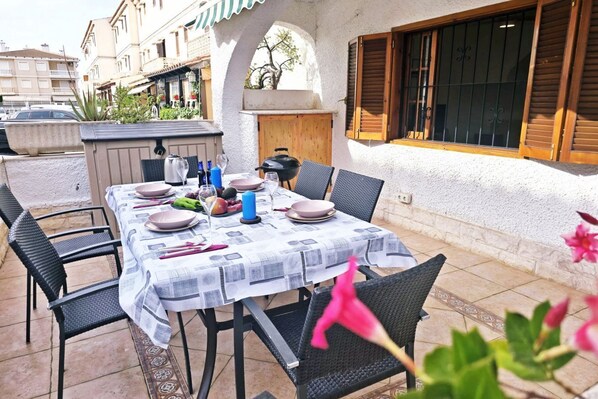 An outdoor dining area with a table set for four, surrounded by chairs, and a view of the street and buildings in the background. - Bright duplex near the beach in Santa Pola – Terrace with side sea viewsCozy duplex apartment for 6 people, located in a quiet residential area, just a few steps from the beach.On the ground floor, you'll find a living room decorated with a mural simul (Santa Pola)