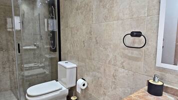 Une salle de bain comprenant des toilettes, une douche en verre, un mur recouvert de carreaux de marbre, un porte-rouleau de papier toilette et un porte-serviettes.