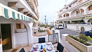 Una terraza con una mesa lista para comer, rodeada de edificios con balcones y una calle al fondo.