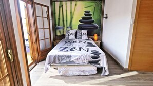 Una habitación con cama, pared decorada con motivos zen, ventilador de techo y puerta de madera.