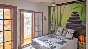 Un dormitorio con cama, ventilador de techo, mesita de noche y vistas al exterior.