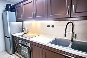 A kitchen with dark wooden cabinets, a stainless steel refrigerator, a double sink, and a stove.