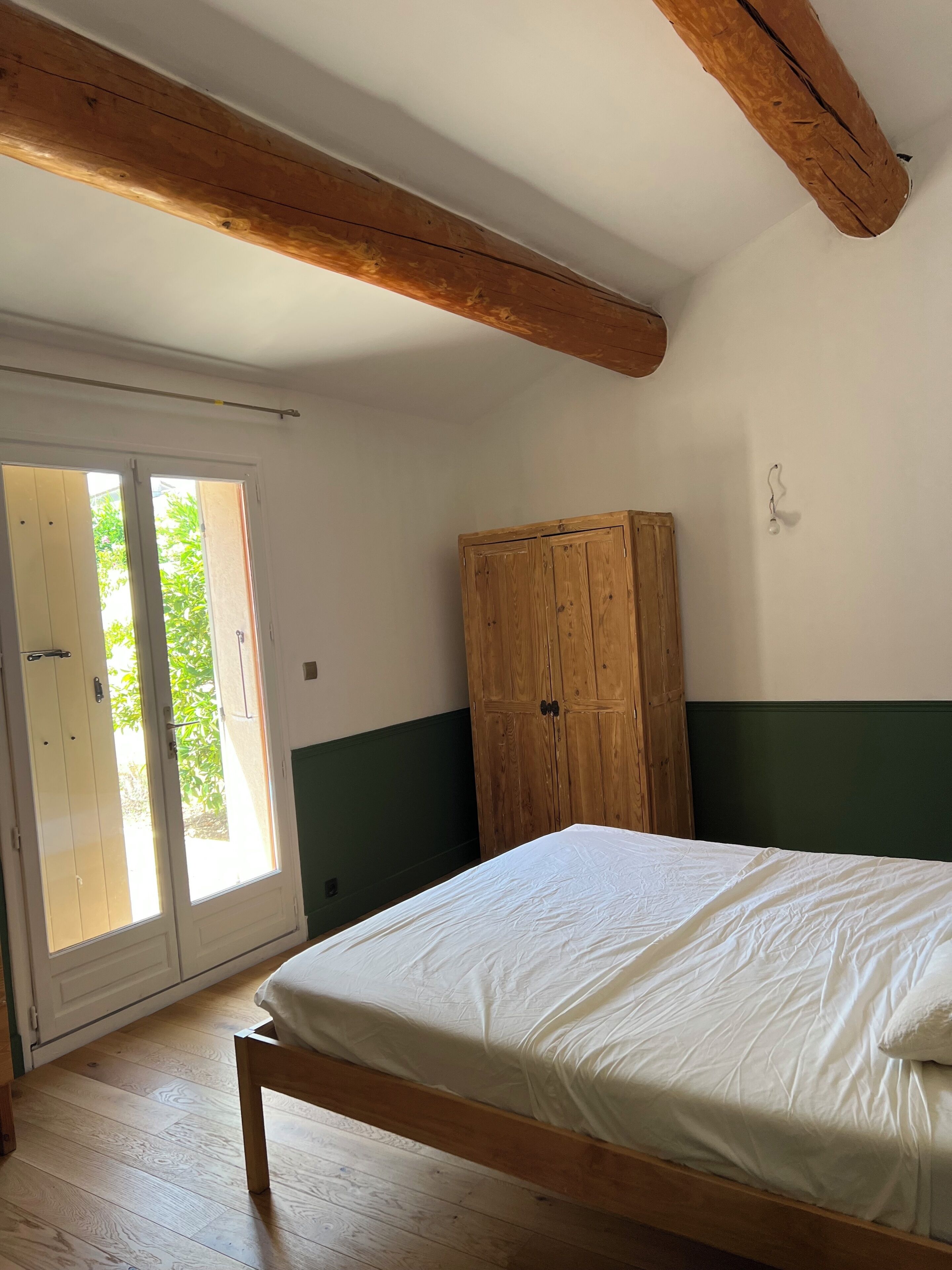 A bedroom with a wooden bed, a wardrobe, and a sliding glass door leading to an outdoor area.