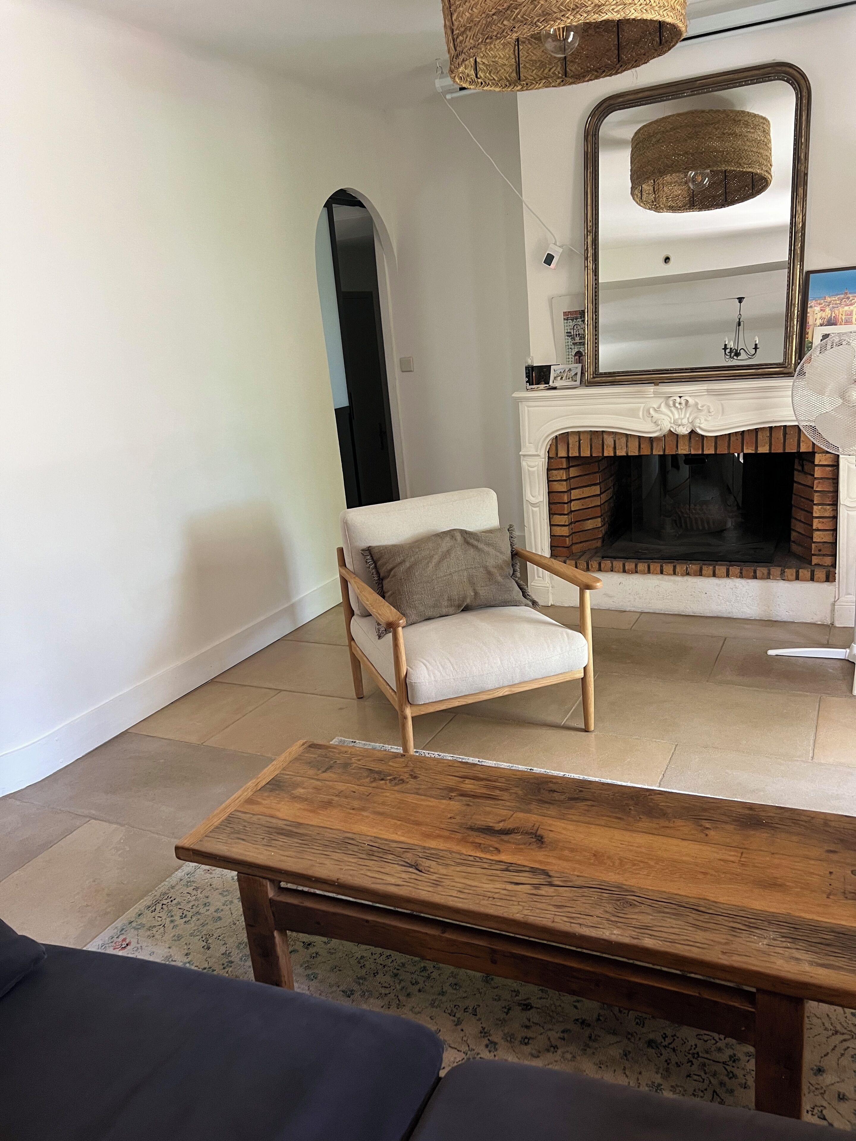 Un salon avec une cheminée, une table basse en bois, un fauteuil confortable et un miroir au-dessus de la cheminée.