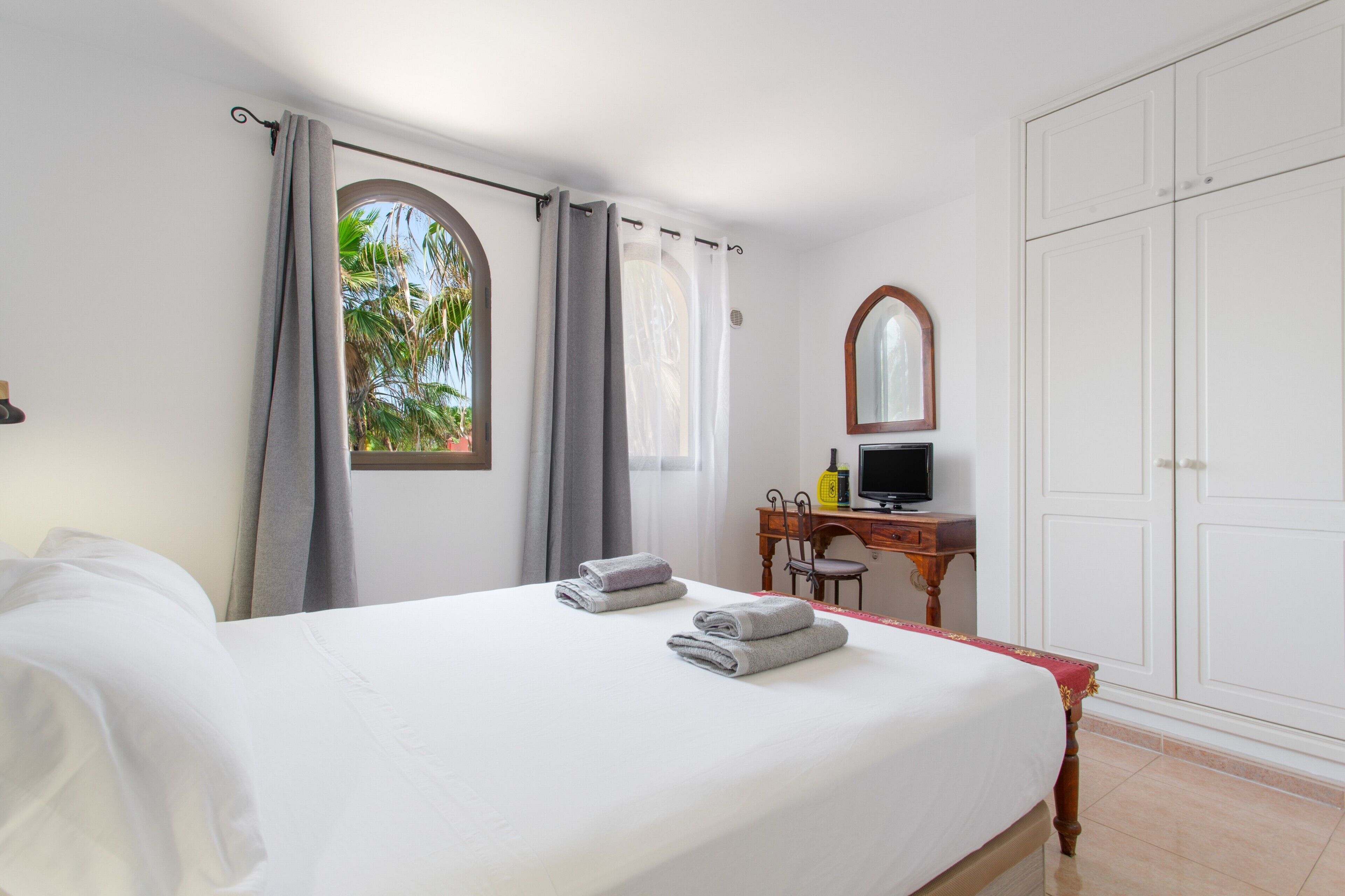 Une chambre d’hôtel avec un lit, un bureau avec un ordinateur, une armoire et une fenêtre avec des rideaux.