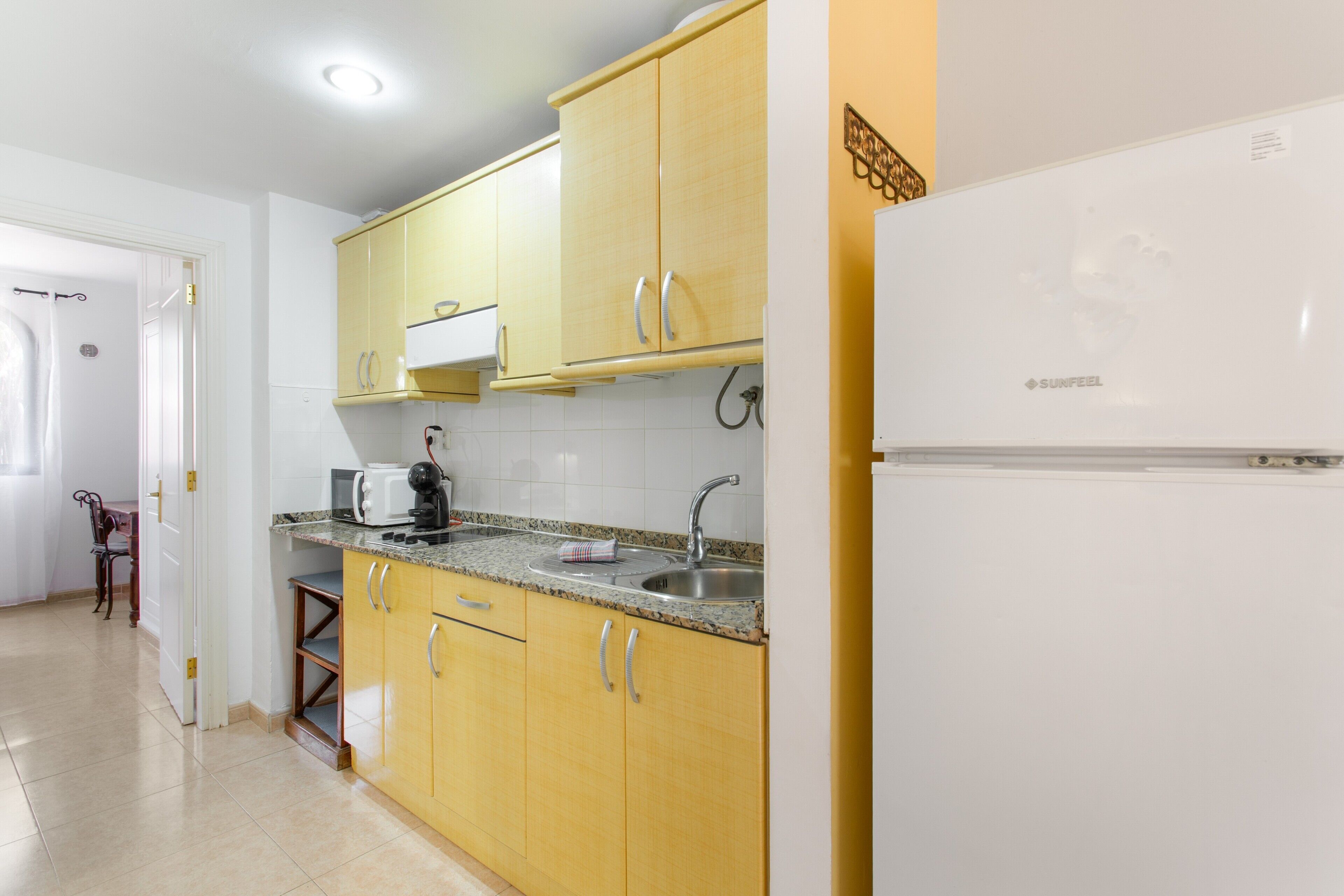 Una cocina con armarios amarillos, un refrigerador blanco, un microondas y un lavamanos.