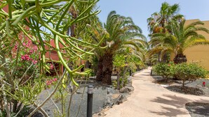 Een pad omzoomd met palmbomen en bloeiende planten, dat naar een gebouw met een rode gevel leidt.