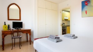 Een hotelkamer met een bed, een bureau met stoel, een televisie, een kledingkast en een schilderij aan de muur.