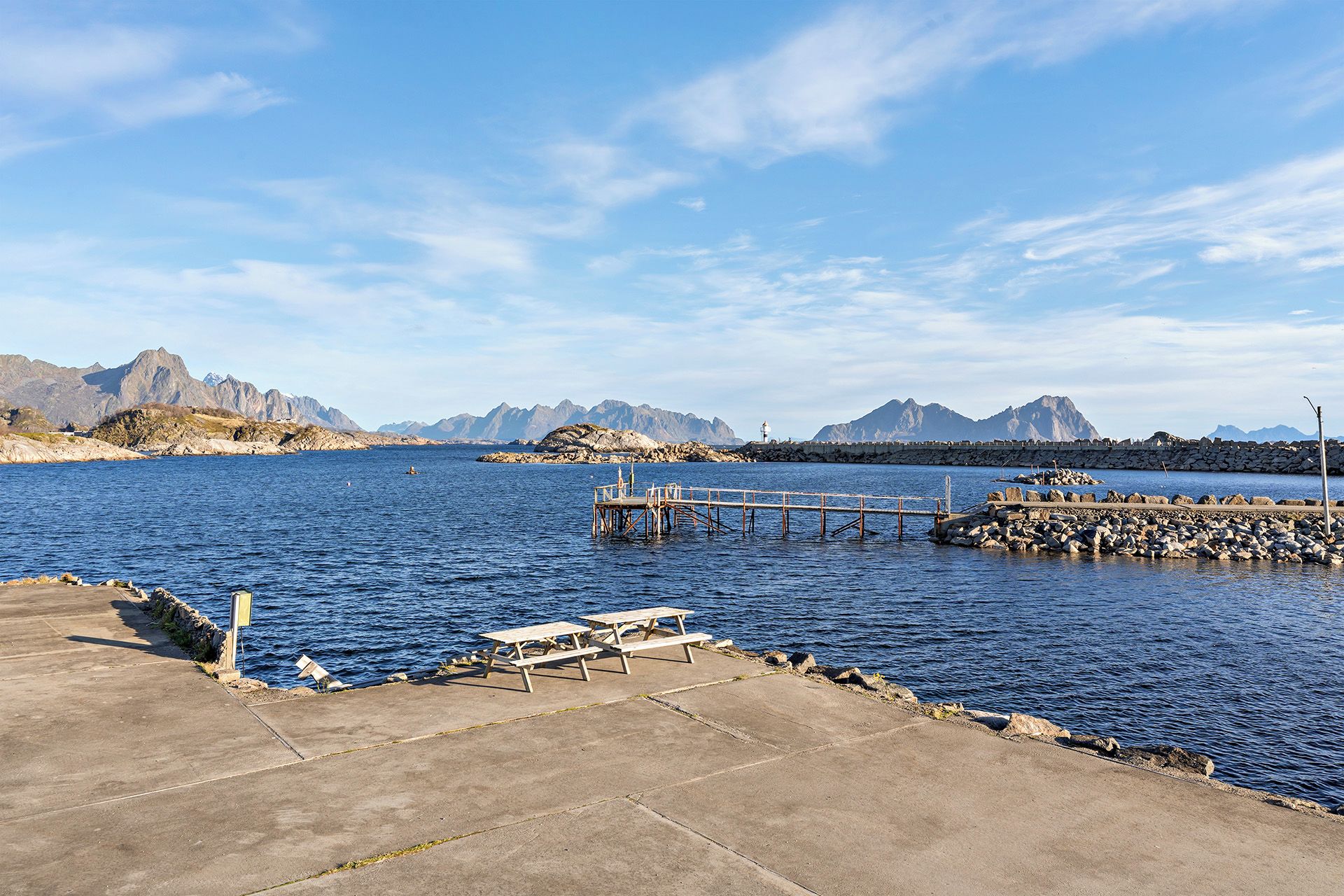 A coastal pier with a picnic table and a lighthouse in the background.