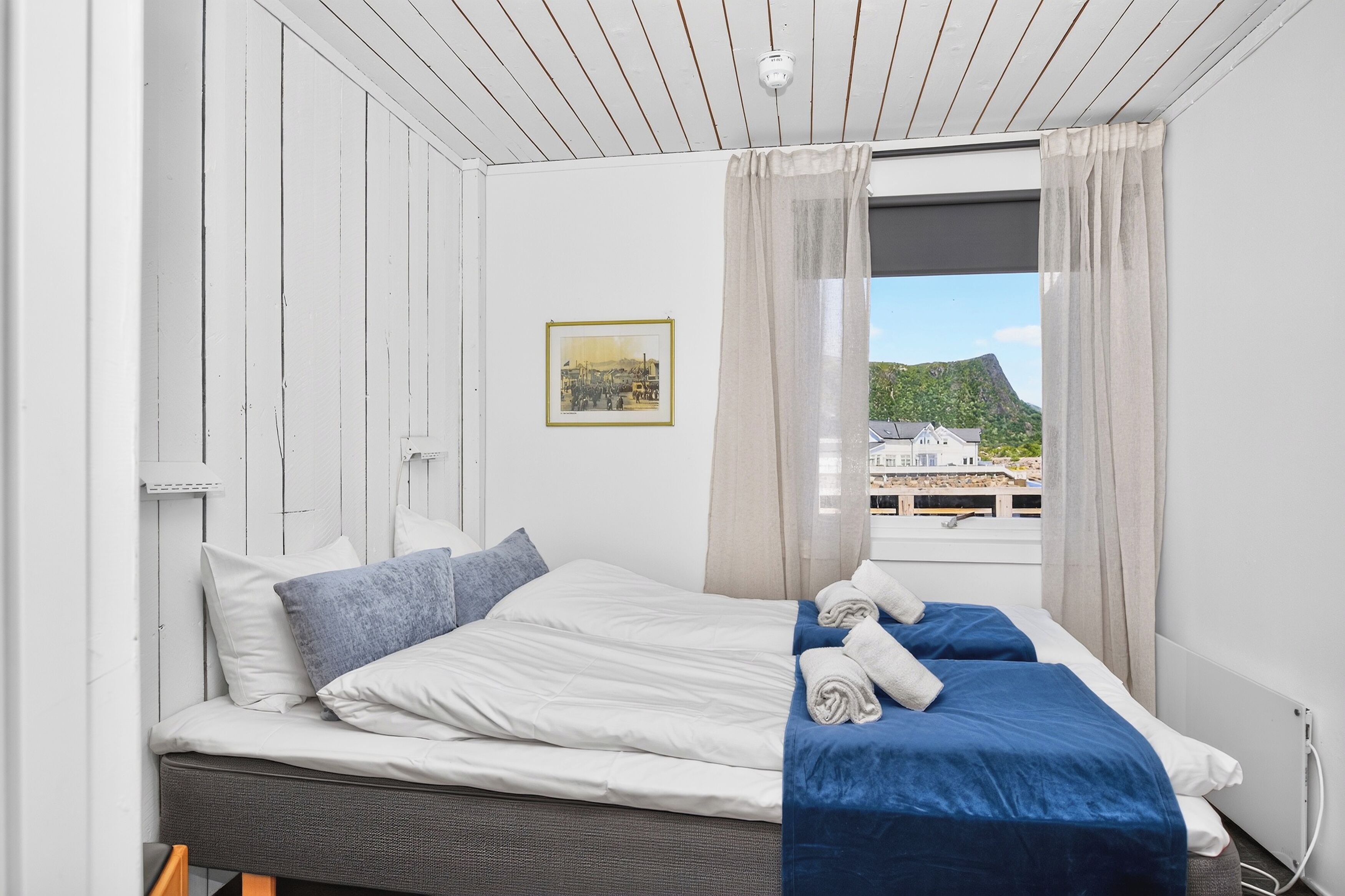 Habitación de hotel con dos camas, una ventana con cortinas, un cuadro en la pared y vistas a un edificio y paisaje.