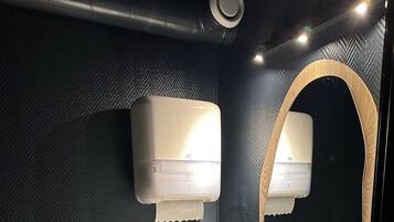 A bathroom with a textured wall, a white sink, a mirror with a wooden frame, and two wall-mounted air dryers.