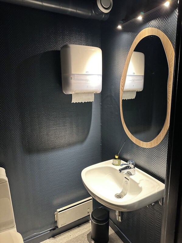 A bathroom with a textured wall, a white sink, a mirror with a wooden frame, and two wall-mounted air dryers.